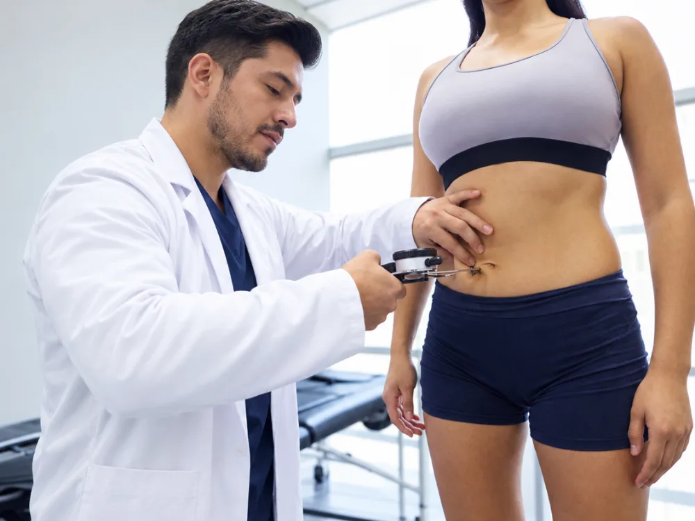 Médico midiendo los pliegues cutáneos a una deportista durante su evaluación en el gimnasio
